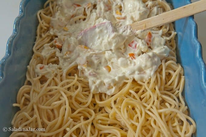 cpreading cream cheese on top of spaghetti.