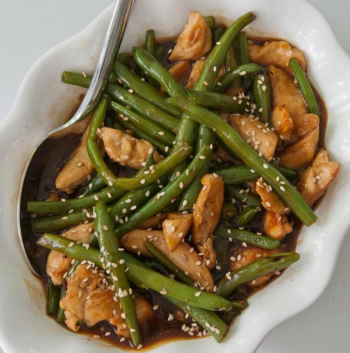 Chinese chicken and green beans in a white serving dish with a spoon.