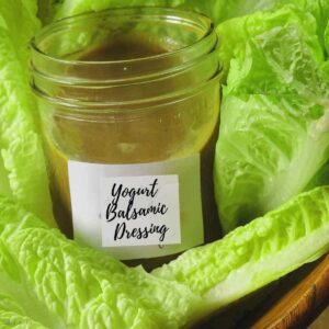 A low-calorie salad dressing recipe flavored with balsamic and yogurt in a jar surrounded by lettuce.
