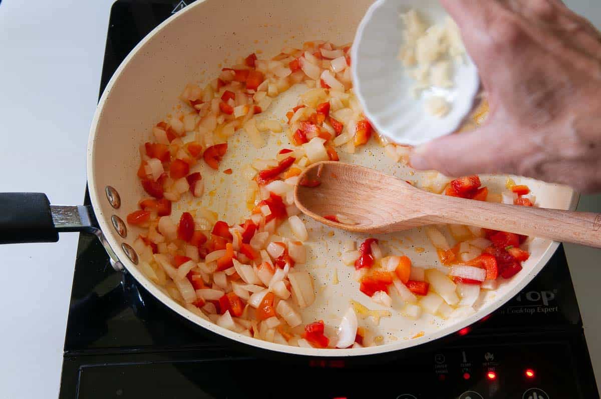 Adding garlic to the onions and bell peppers