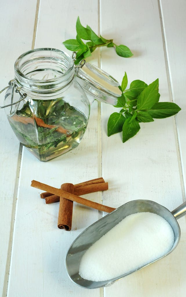 CINNAMON BASIL SYRUP in a jar with cinnamon sticks and sugar in a scoop