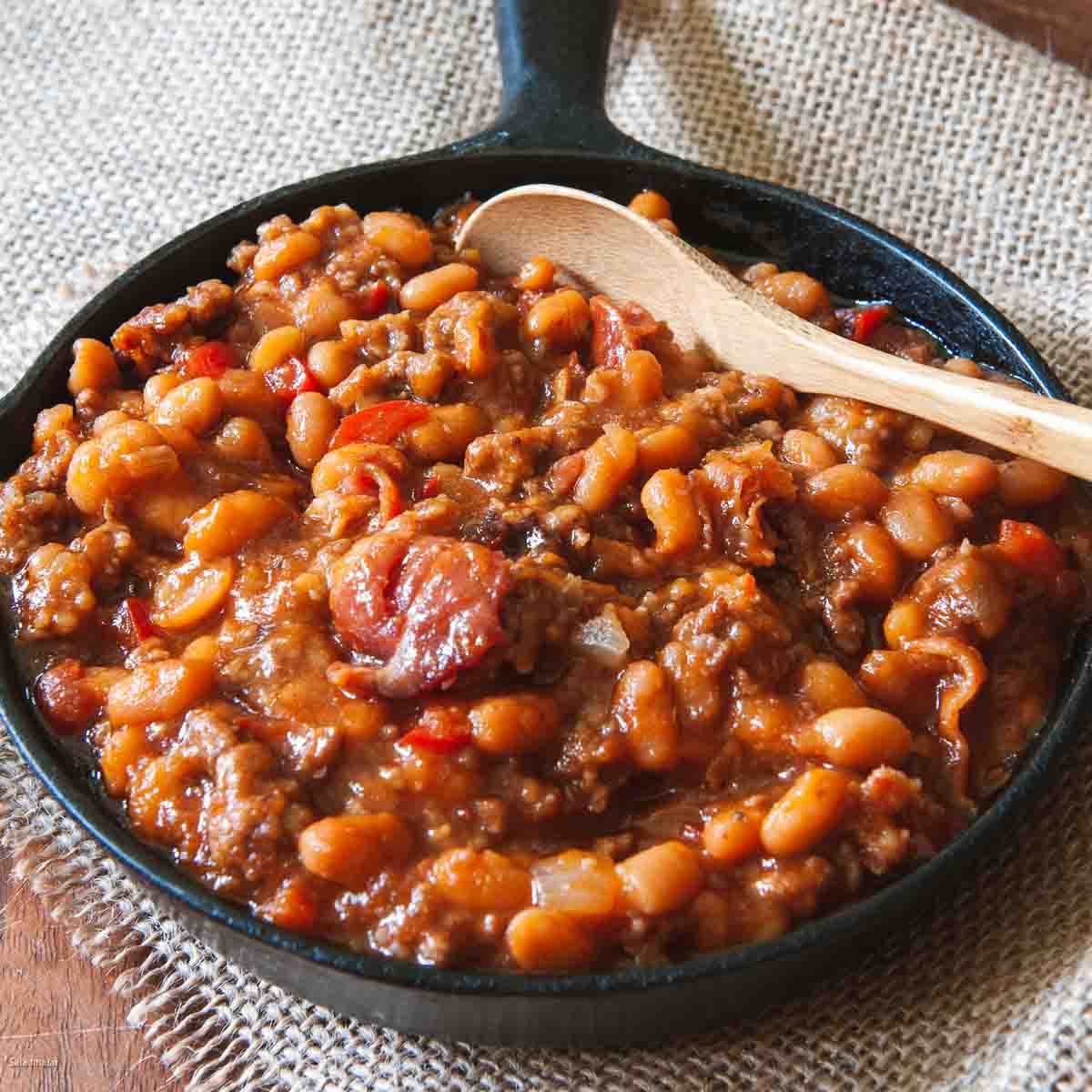 baked beans with hamburger in a black skillet with wooden spoon