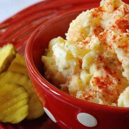 potato salad in a bowl with pickles on the side.