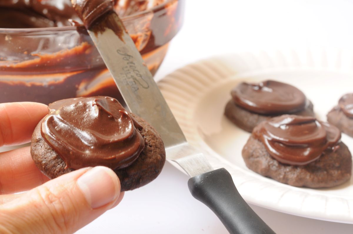 applying chocolate frosting to chocolate cookies