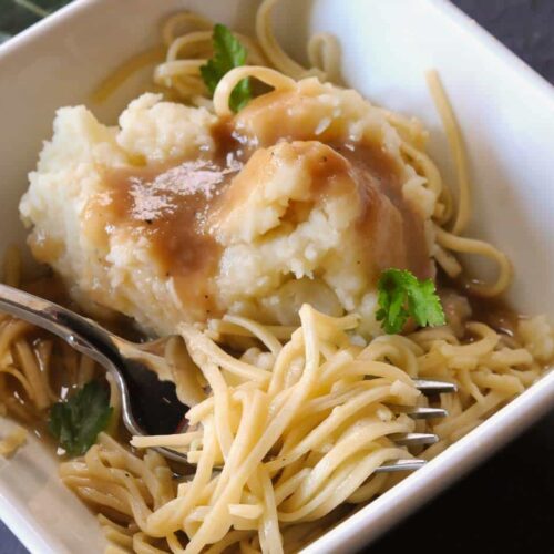 Egg noodles in a square bowls with mashed potatoes and gravy.