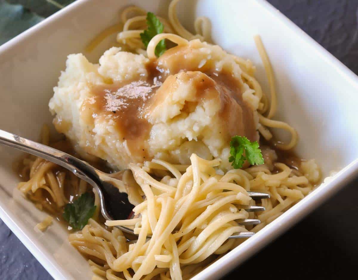 Egg noodles in a square bowls with mashed potatoes and gravy.