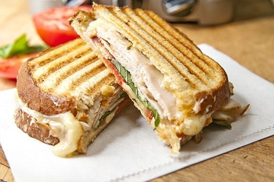 SMOKED TURKEY, PEPPER JACK CHEESE, AND BASIL PANINI - sliced in half with tomato in the background