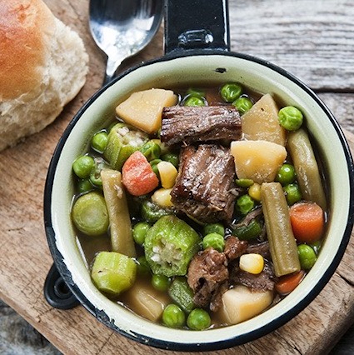 beef and vegetable soup without tomatoes in a small pan with a roll on the side.