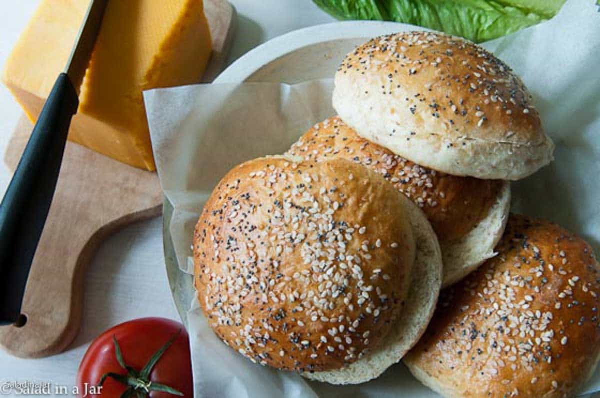 Multigrain burger buns in a bowl next to a chunk of cheese ready to make sandwiches.