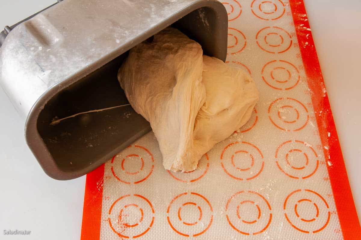 Pulling the dough out of the bread machine pan onto a silicone mat in preparation for shaping by hand.