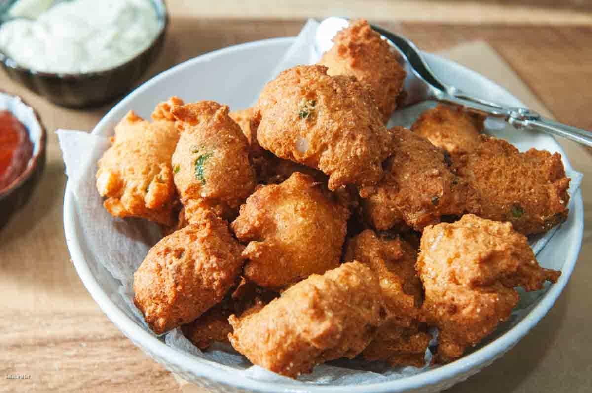 fried hushpuppies on a plate with tartar sauce and cocktail sauce on the side