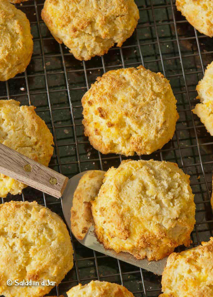 Keto yogurt biscuits on a cooling rack with a spatula lifting one of them