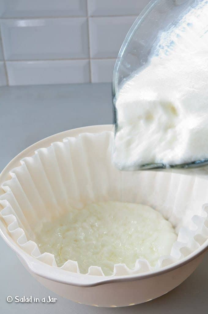 Pouring set yogurt into a coffee filter-lined plastic colander.