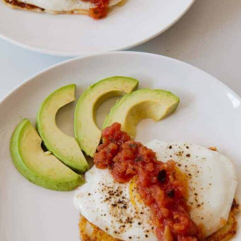 fried egg on top of fried cheese garnished with avocados and salsa