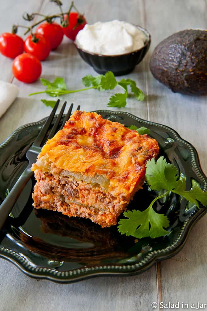 serving of Baked Chili Relleno Pie on a plate with cherry tomatoes, sour cream and avocado in the background.