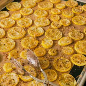 Oven roasted yellow squash with parmesan on a cookies sheet with tongs