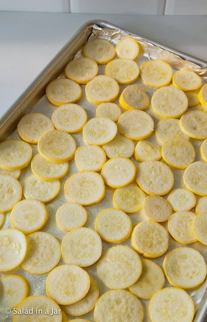Sliced yellow squash arranged on covered baking sheet with no oerlap.