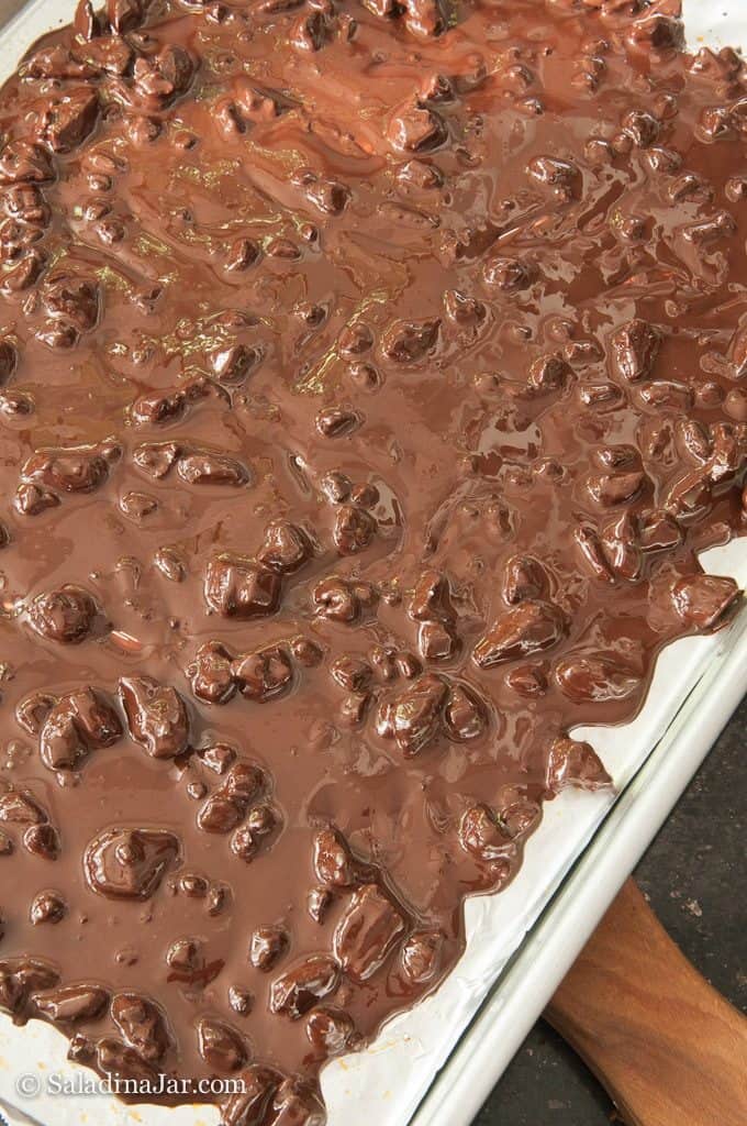 Melted chocolate with pecans spread on a wax-paper-lined cookie sheet