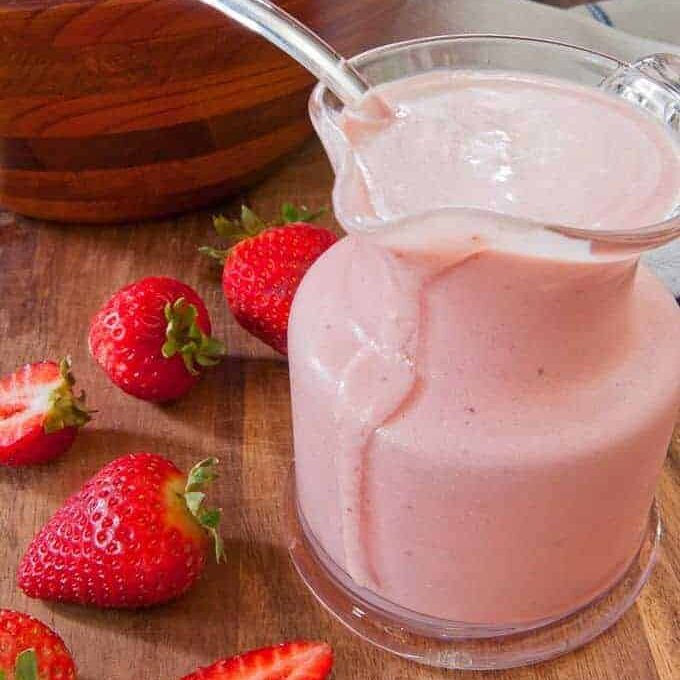 Creamy Strawberry Salad Dressing sitting beside spinach salad and strawberries