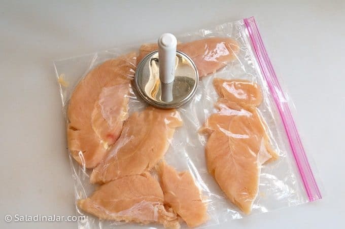 Raw chicken tenders in a plastic ziplock bag with a meat pounder