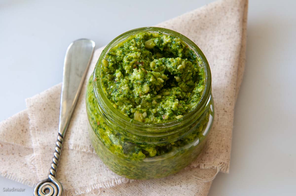 homemade cilantro pesto in a jar with a spoon on the side