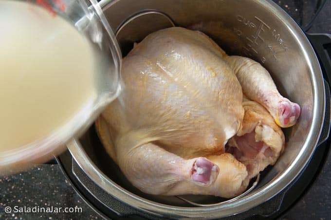 Pouring broth over whole chicken in the Instant Pot