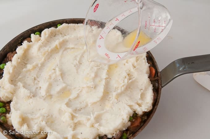 pouring butter over mashed potato layer