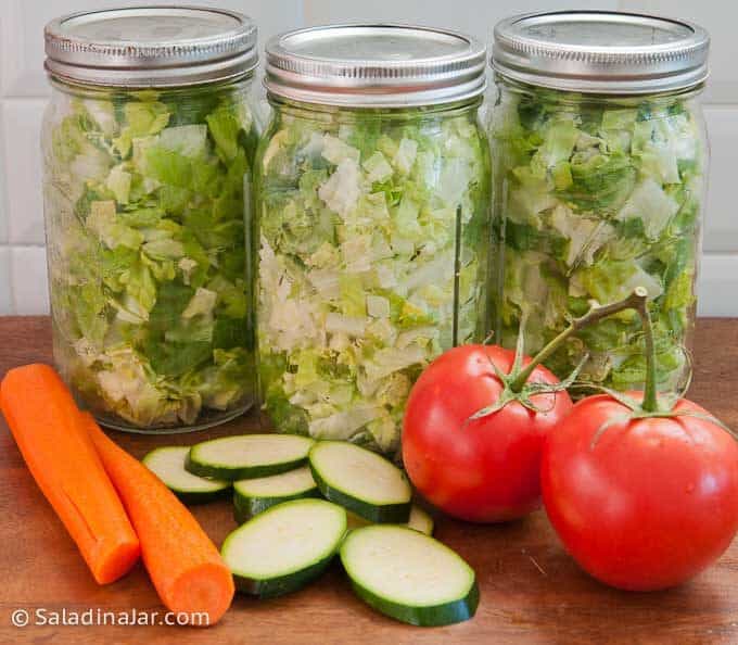 vacuum-sealed jars of lettuce with fresh veggies laying next to them