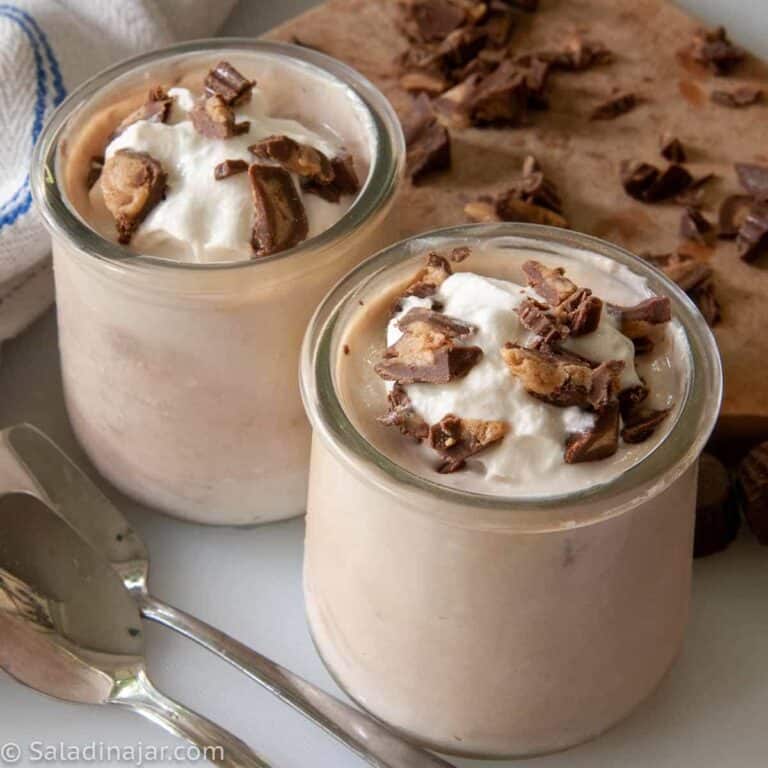two cups of peanut butter cup yogurt with chopped peanut butter cups on top and spoons on the side.