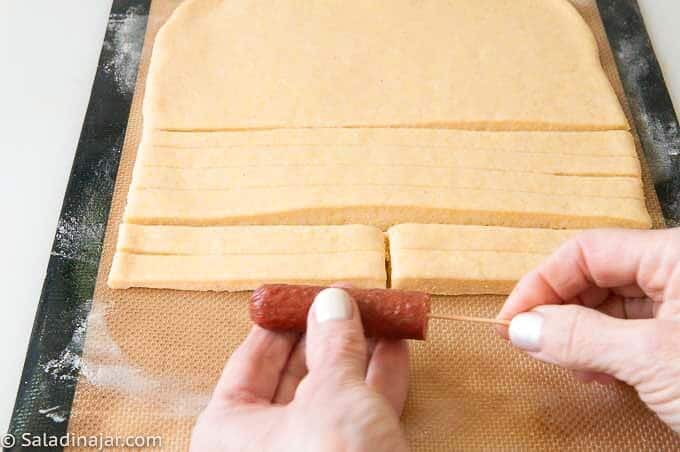 Cut each strip in half and each hot dog in half. Sticking a toothpick in one end of the hot dog is optional.