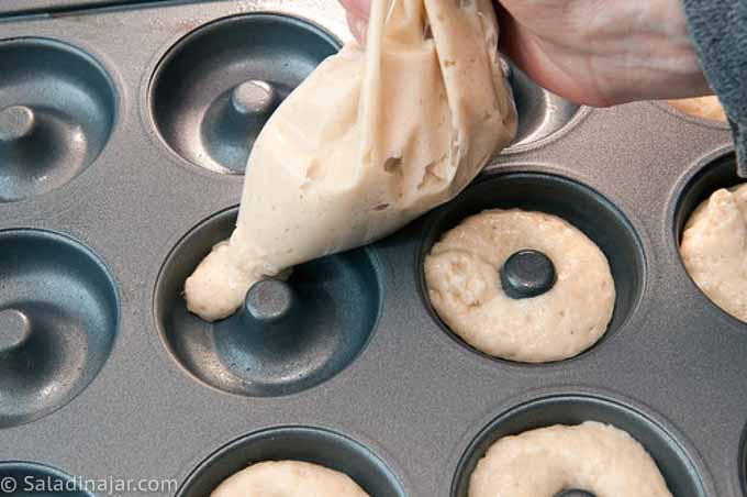 Filling donut pans with dough squirted out of  a plastic bag