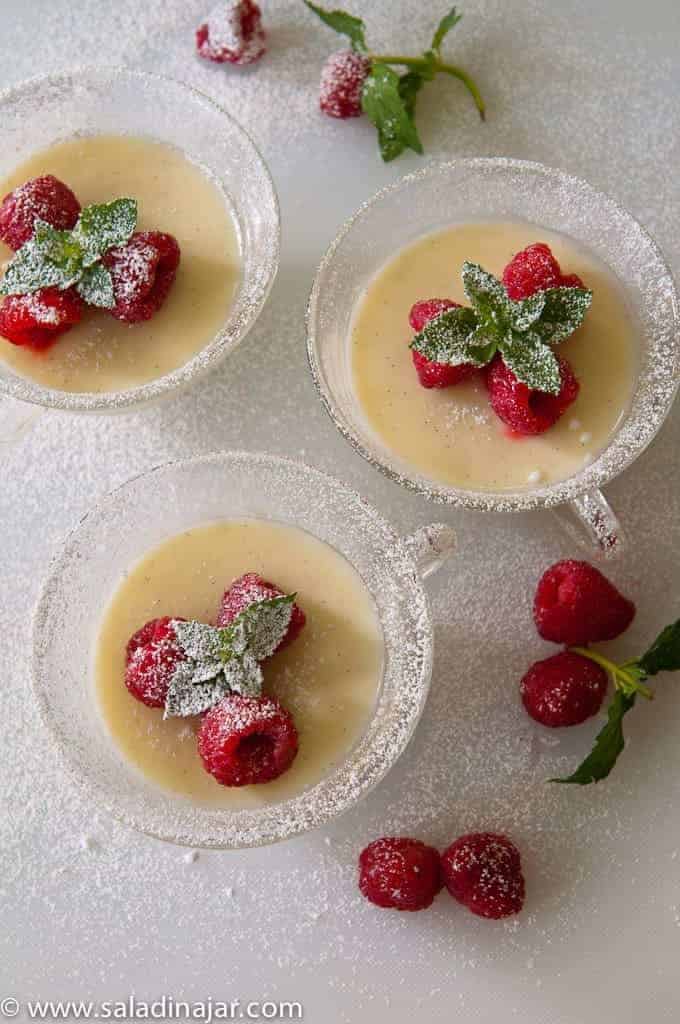 vanilla posset in serving dishes, garnished with raspberries, sprinkled with powdered sugar