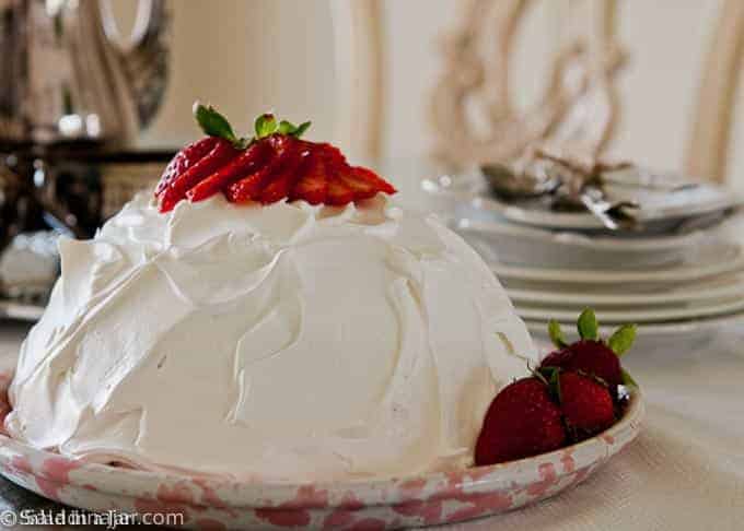 uncut torn angel food cake covered with whipped cream and garnished with strawberries