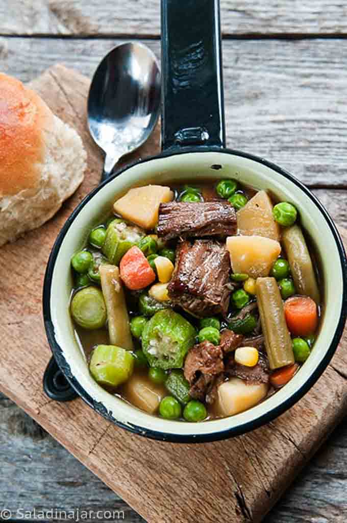 VEGETABLE BEEF SOUP in a pot next to a spoon and a roll