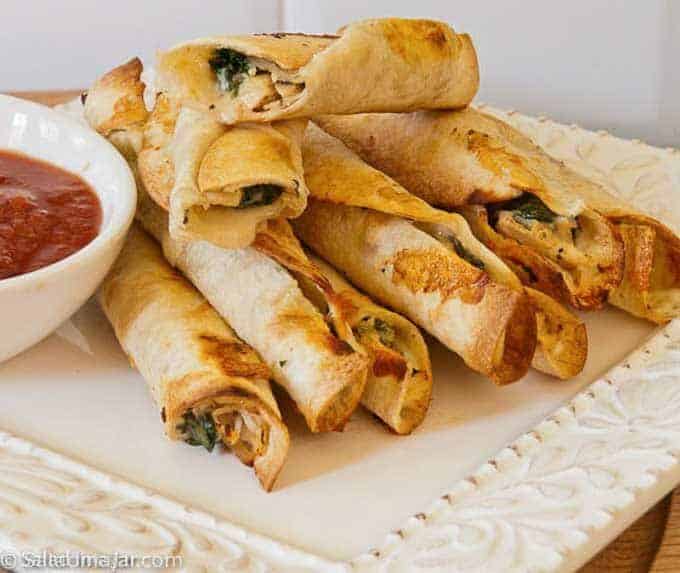 chicken and spinach flautas on a serving tray with salsa