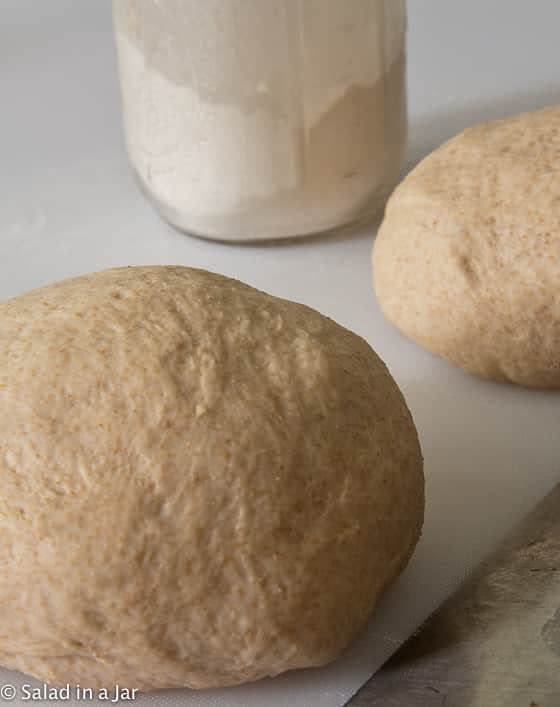 two balls of honey wheat pizza dough and a jar of flour
