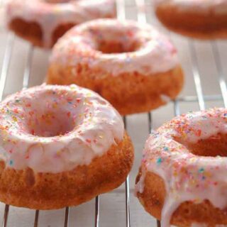 strawberry donuts with sprinkles on a wire rack.