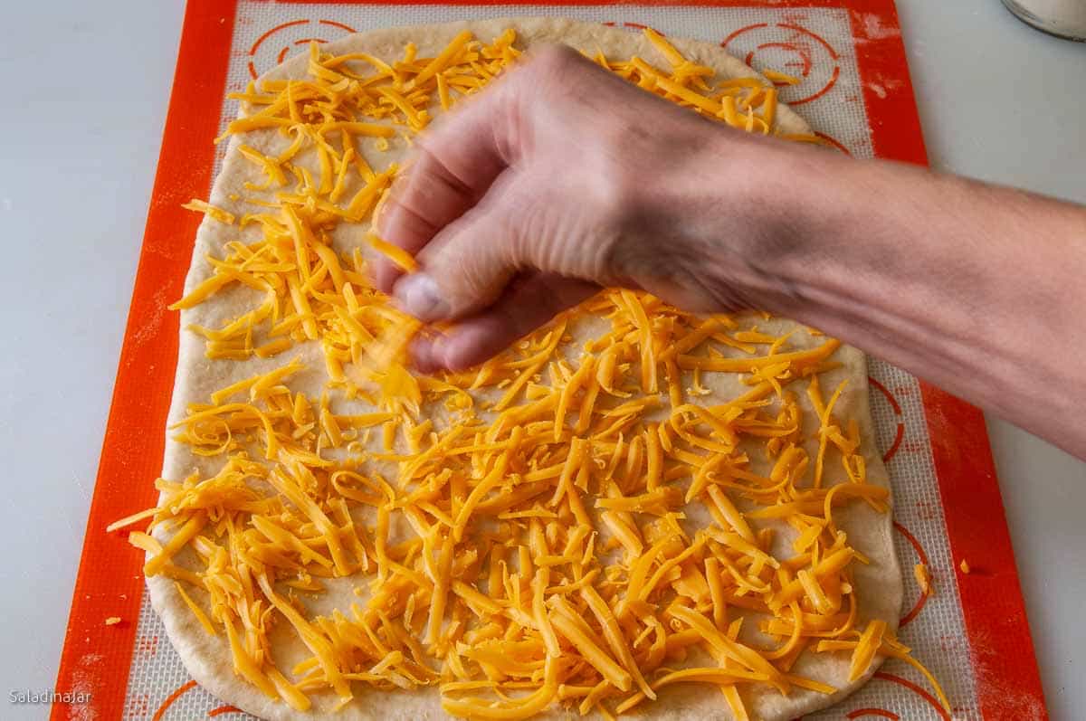 Sprinkling cheese over the rectangle of dough with fingers.