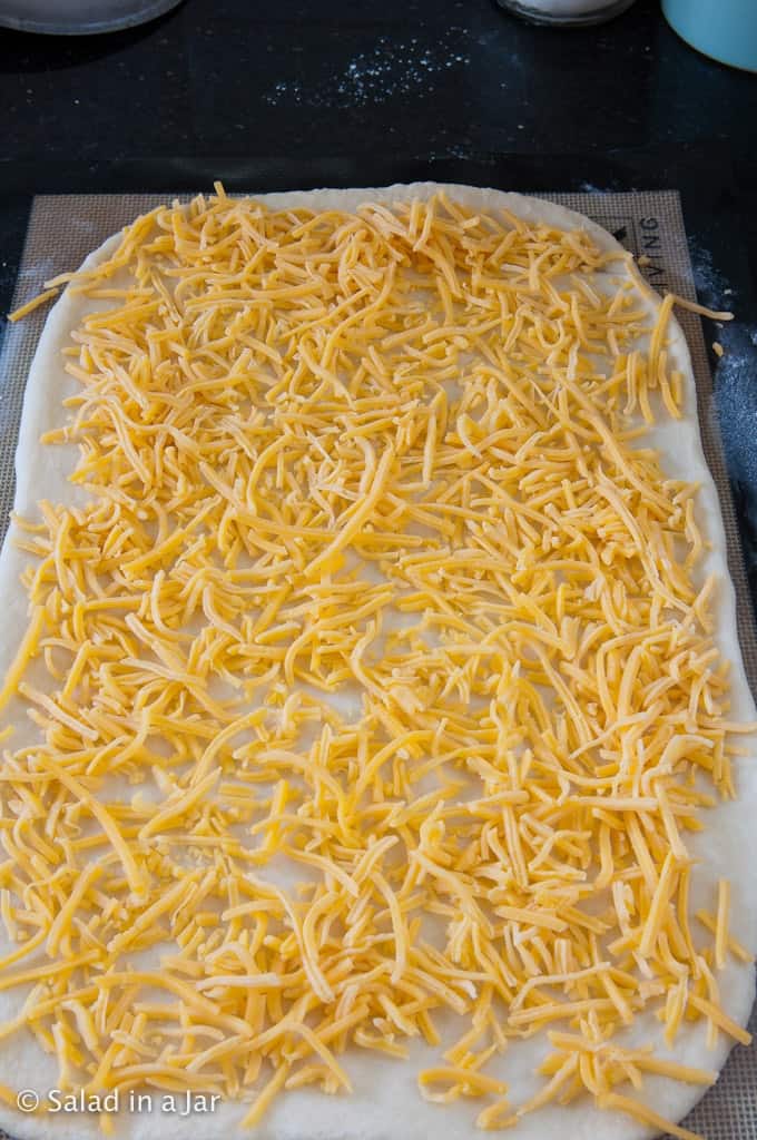 Covering dough with shredded cheese