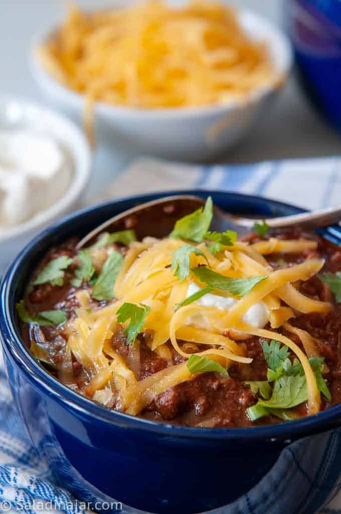 a bowl of beefy chili with a spoon and condiments