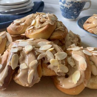 Bear Claws sprinkled with almonds on baking paper with empty dishes in background.