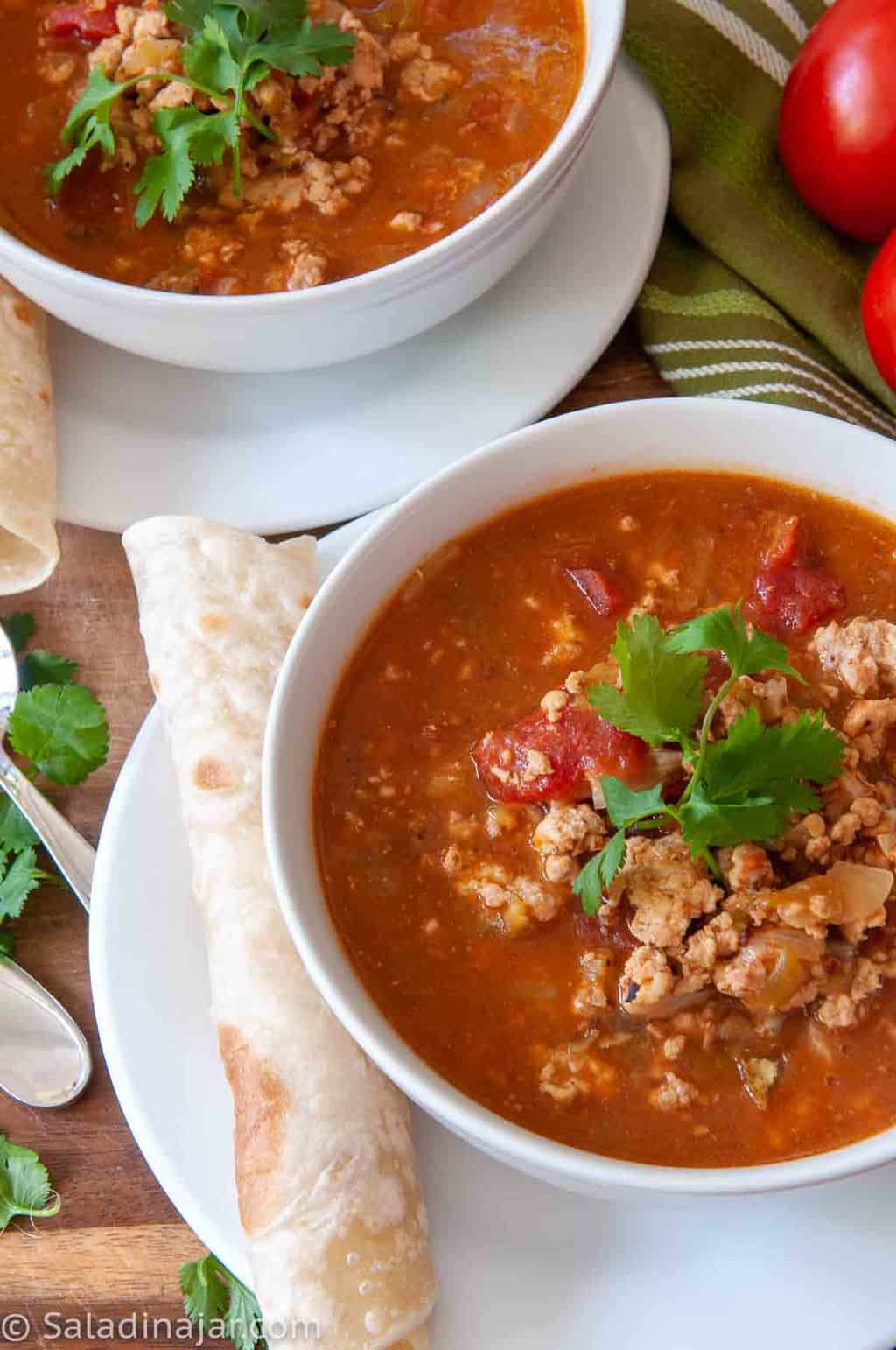 two bowls of green chili stew served with flour tortillas on the side