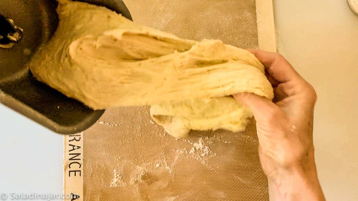 pulling dough out of the bread machine pan onto a floured surface