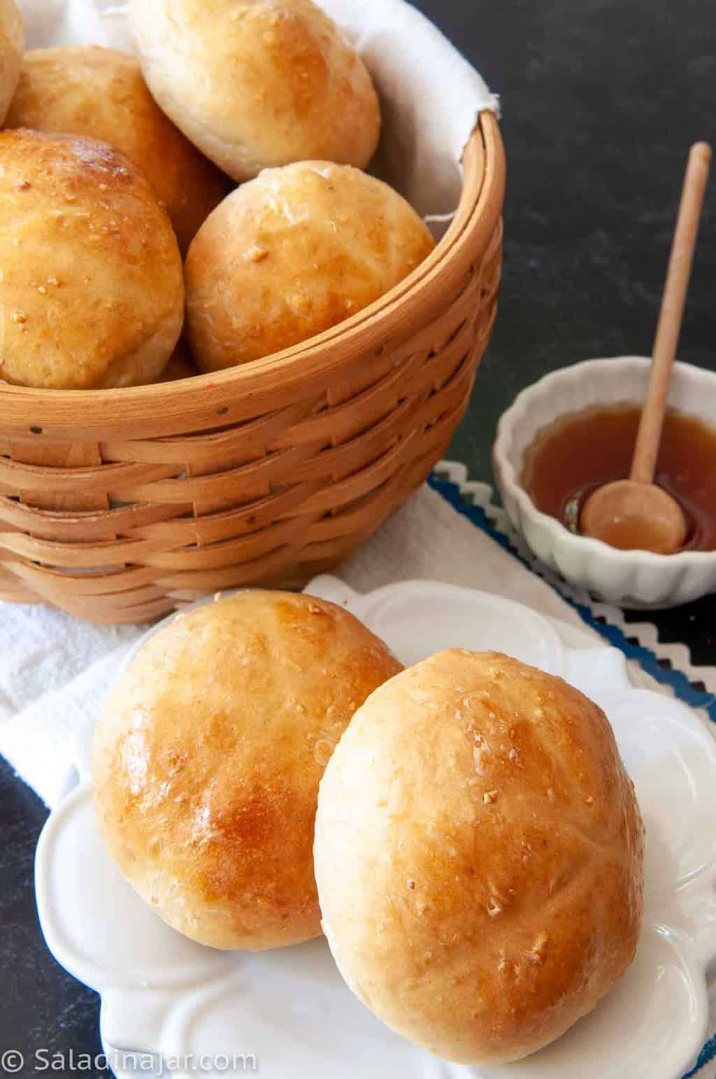 Honey-Kissed Oatmeal Rolls in a basket with honey on the side.