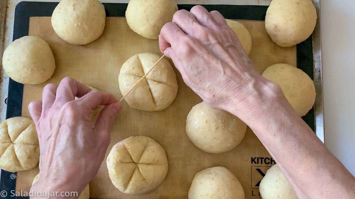 using a wooden pick to make lines across the top of honey oat rolls