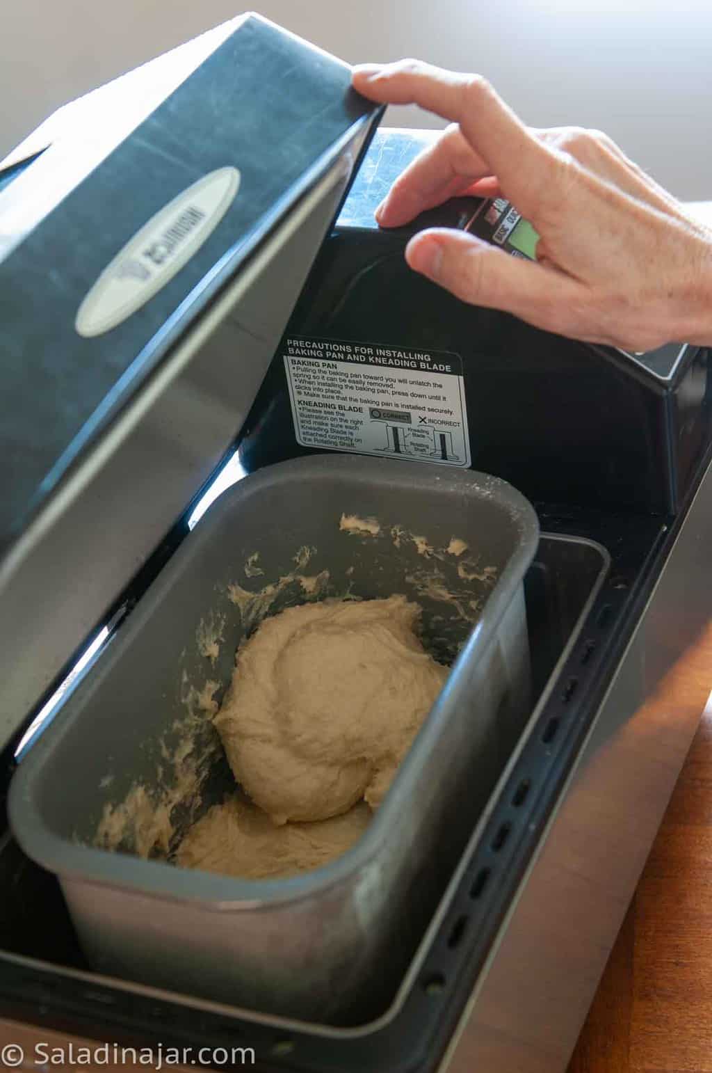 Opening the lid of a bread machine to check the consistency of the dough
