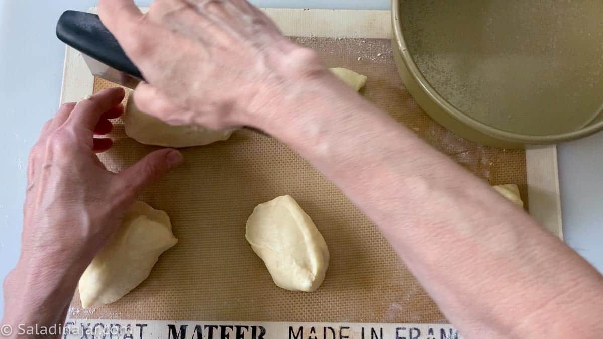 Dividing the original dough ball in two with a bench scraper, then dividing each ball into 8 pieces