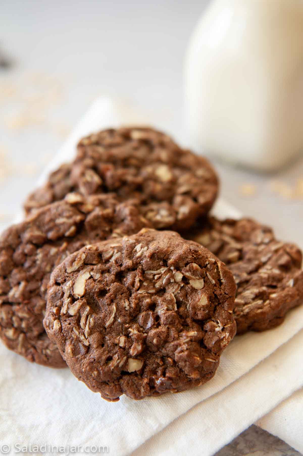 Refrigerator Chocolate Oatmeal Cookies stacked on a plate with milk in the background 