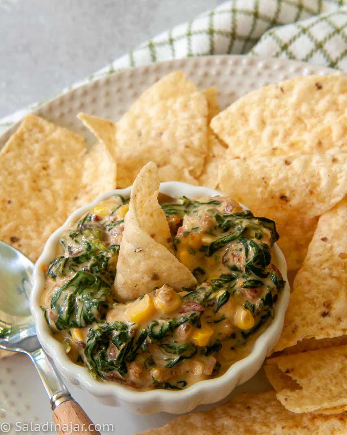 Serving Espinaca as a dip. Shown with tortilla chips surrounding dip on a plate with a spoon.