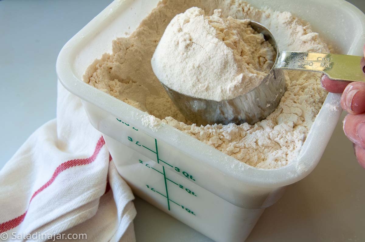 Using a measuring cup to scoop up the flour in a canister